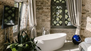 A modern bathroom with a freestanding bathtub, a large window with a view of greenery, and a potted plant.
