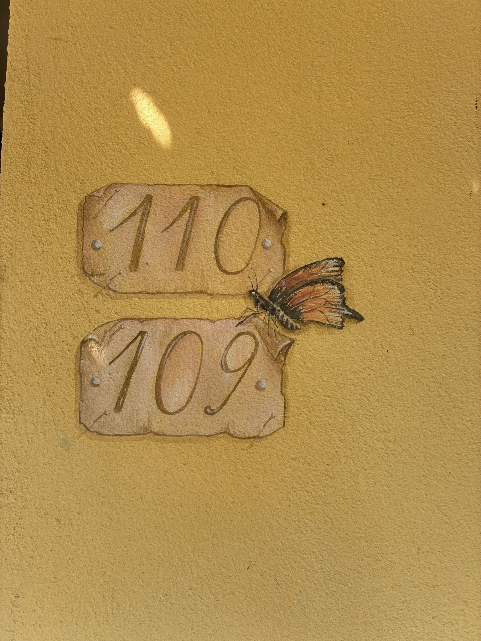 Dos placas de madera con los números '110' y '109' sobre una pared amarilla.