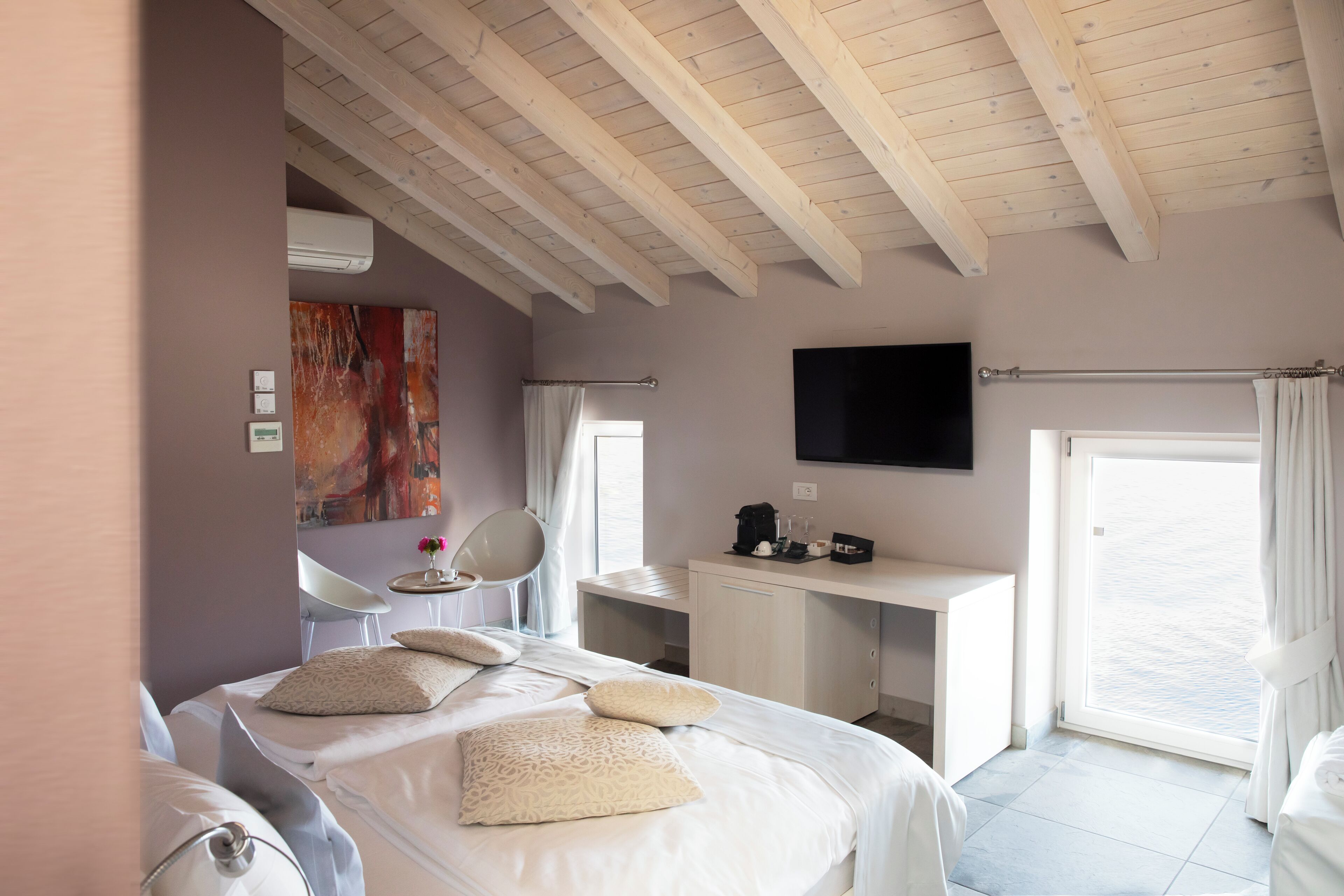A modern hotel room with a large bed, a desk, a flat-screen TV, and a view of the sea through a sliding door.