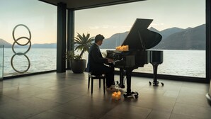 A piano in a spacious room with a large window overlooking a body of water and mountains. - Relais Villa Porta (Luino)