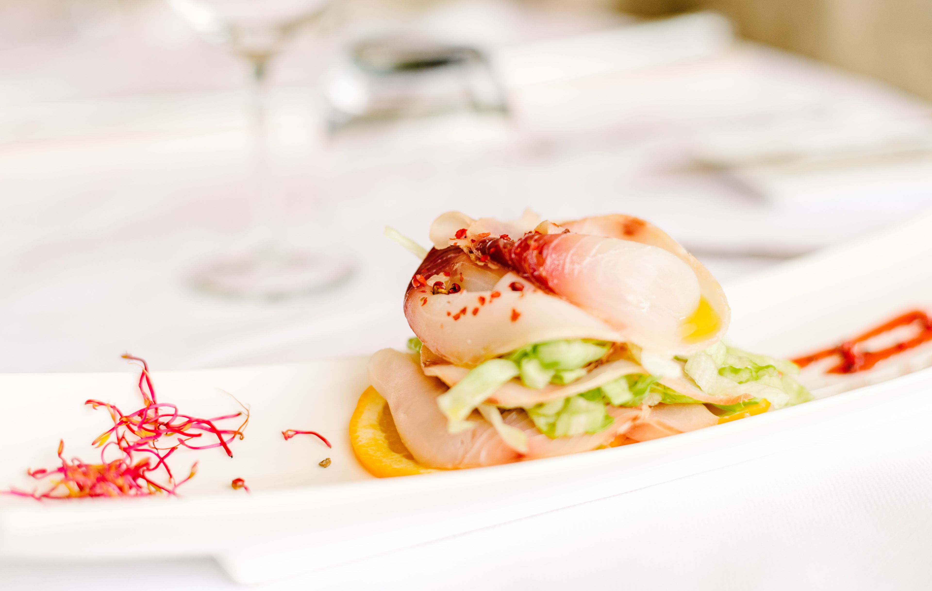 A white plate with a seafood dish, garnished with red chili flakes and a lemon slice.