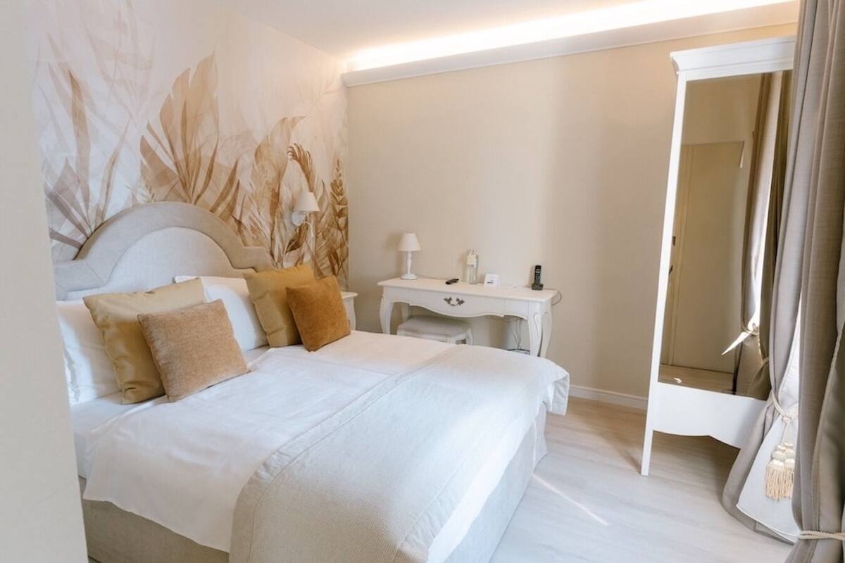 Ein Hotelzimmer mit Bett, Schreibtisch, Spiegel und Wand mit Blätermotiv.