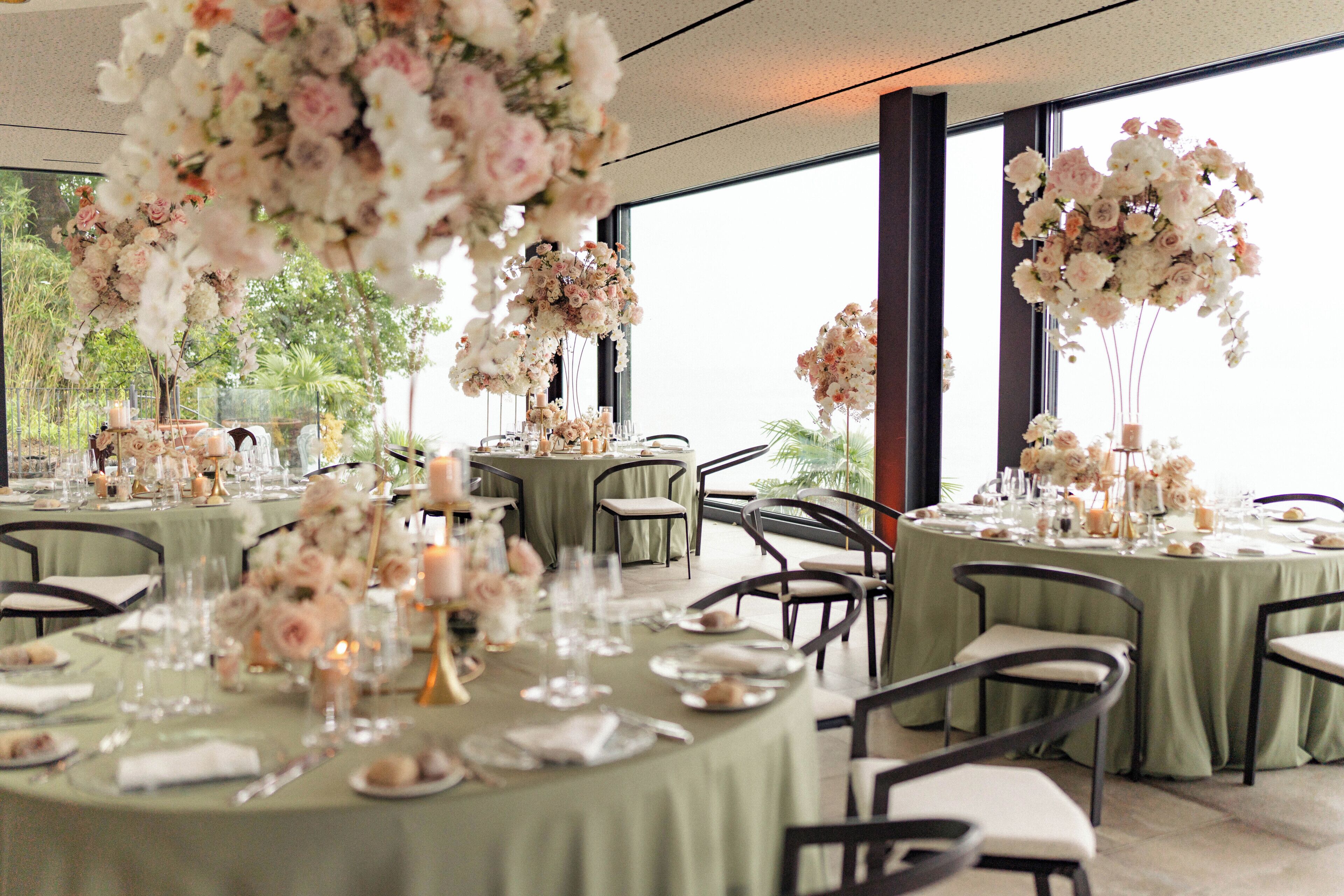 Un salón de banquetes con mesas redondas dispuestas para comer, decorado con arreglos florales y velas.
