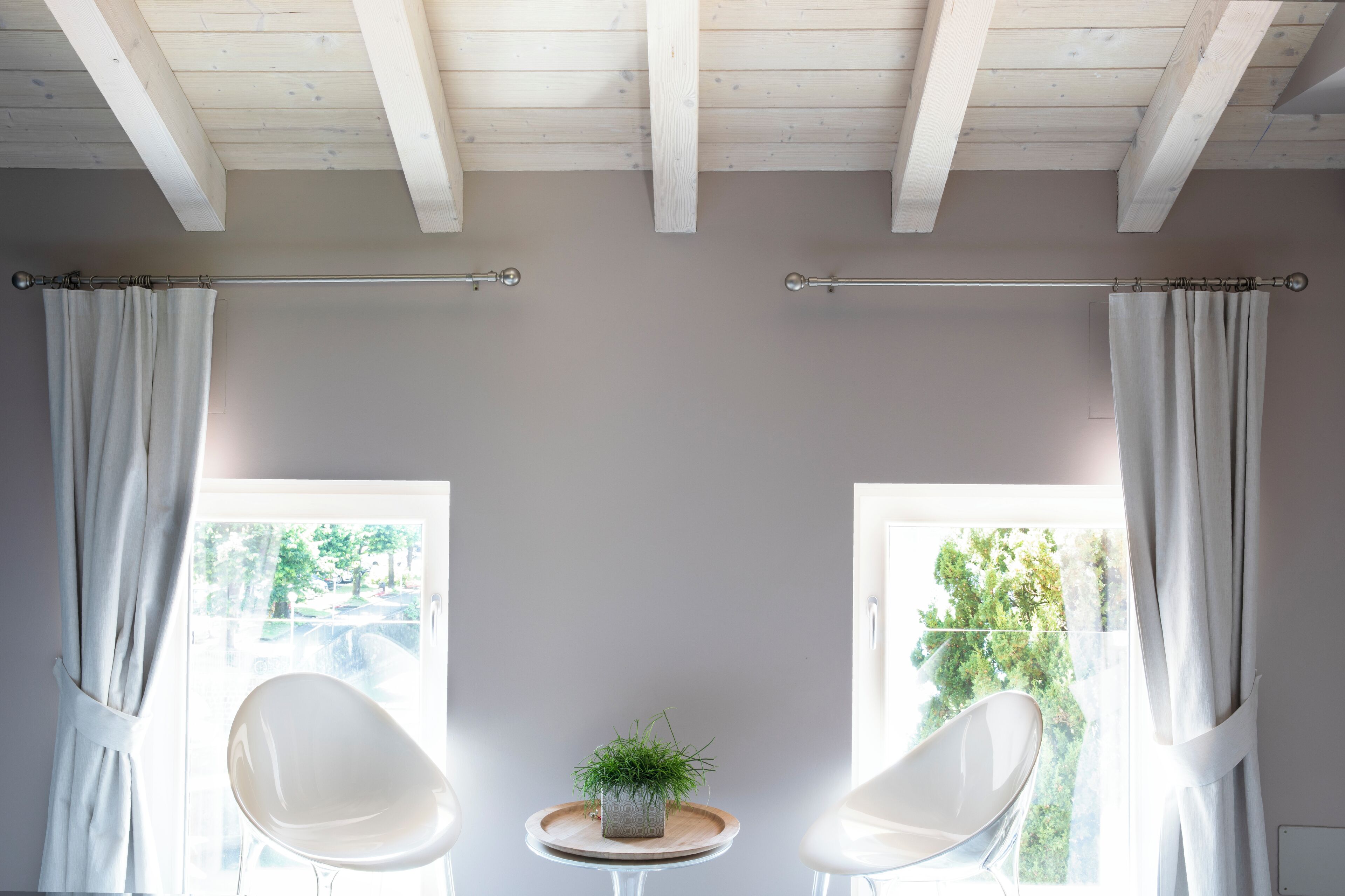 A room with a high ceiling, two white chairs, a small table with a plant, and a view of greenery outside.