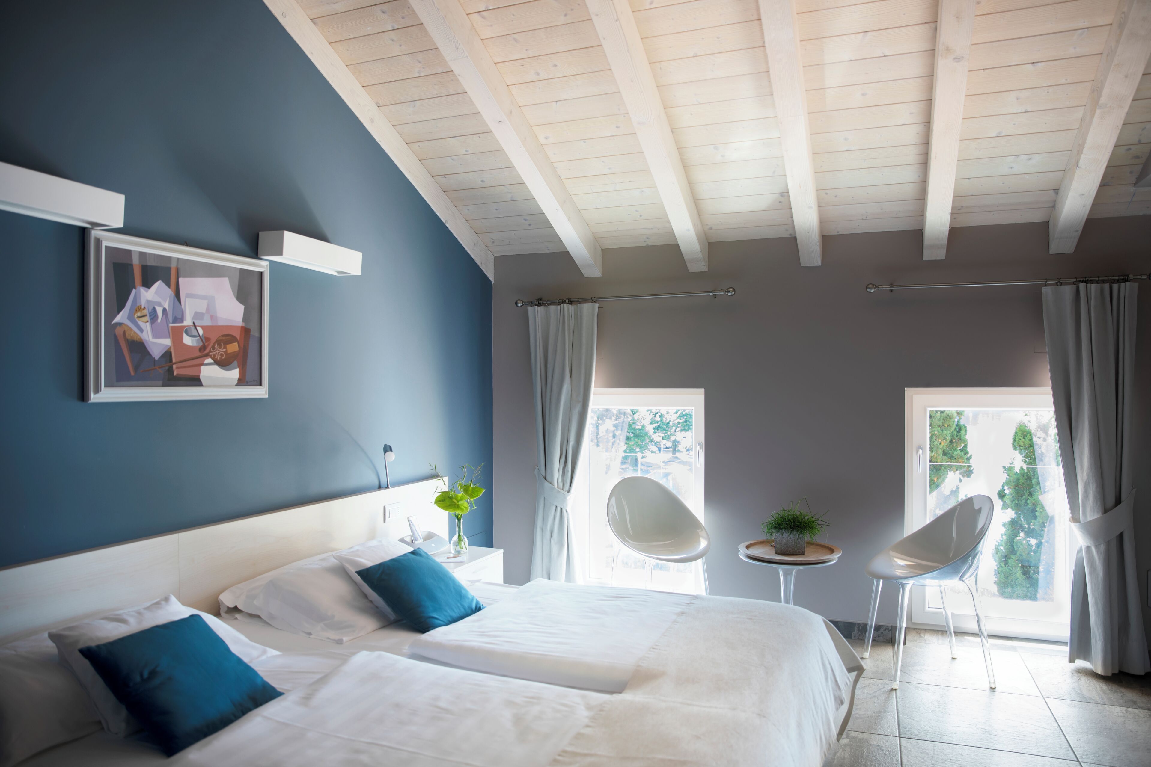 A bedroom with two beds, a window with curtains, a small table with a plant, and a chair.