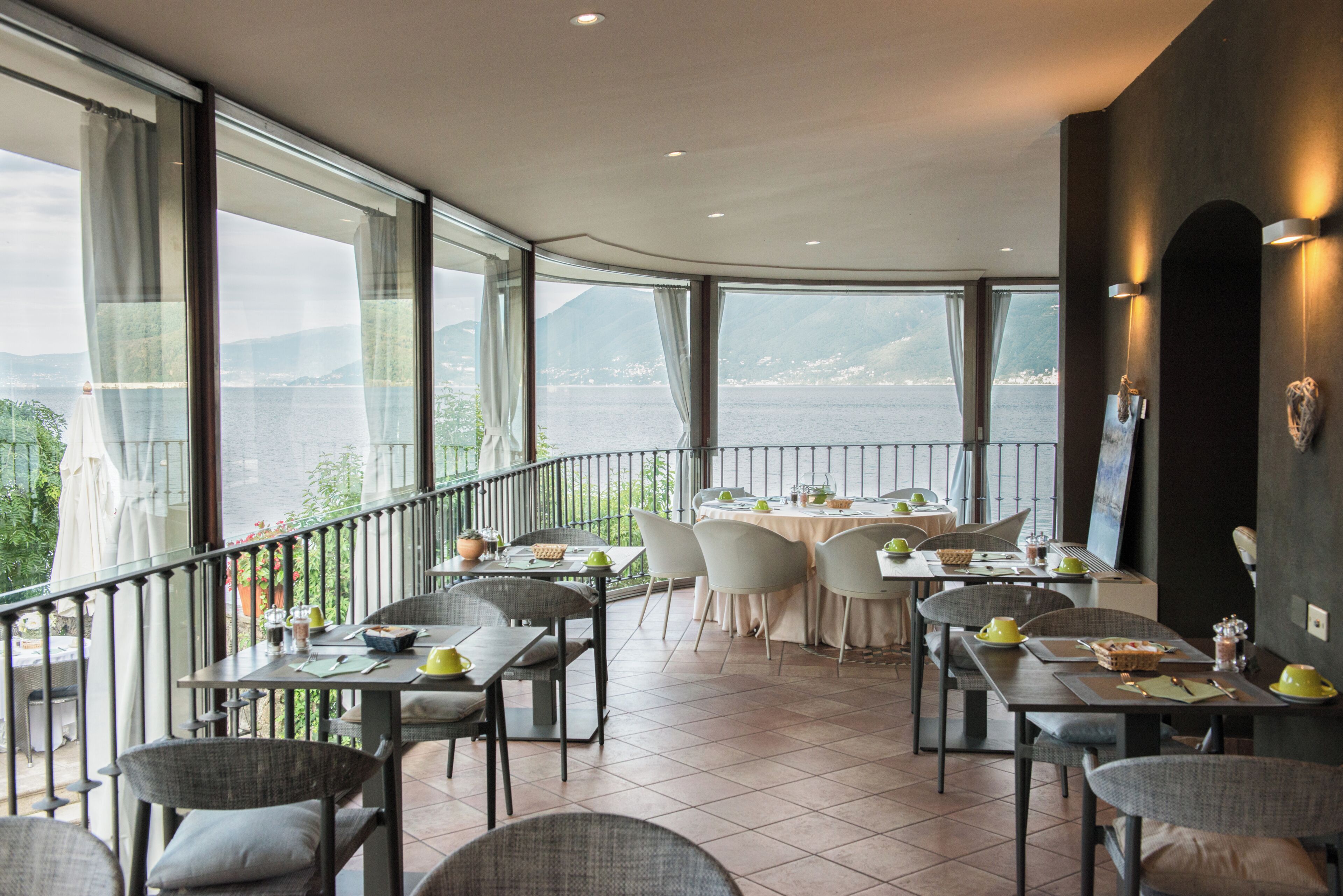 Un restaurant doté d’une terrasse offrant une vue sur un plan d’eau et des montagnes, avec des tables et des chaises disposées pour accueillir les clients.