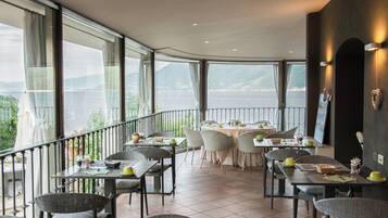 Un restaurant doté d’une terrasse offrant une vue sur un plan d’eau et des montagnes, avec des tables et des chaises disposées pour accueillir les clients.