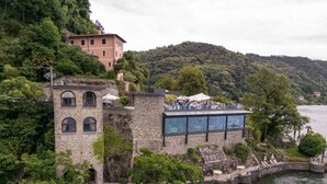 A historic stone building with a terrace overlooking a lake, surrounded by lush greenery and hills. - Relais Villa Porta (Luino)