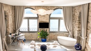 A modern bathroom with a large bathtub, a desk with a computer, a potted plant, and a view of the sea through large windows. - Relais Villa Porta (Luino)