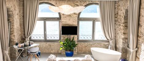 Une salle de bain moderne avec une grande baignoire, un bureau avec un ordinateur, une plante en pot et une vue sur la mer grâce à de grandes fenêtres.