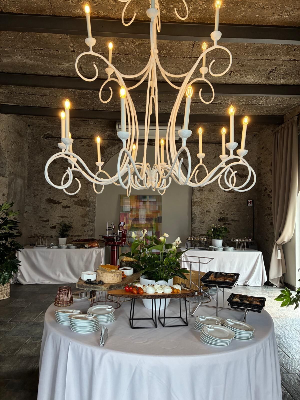 Un salón de banquetes con una gran lámpara de araña, mesas redondas con manteles blancos y una mesa de buffet.