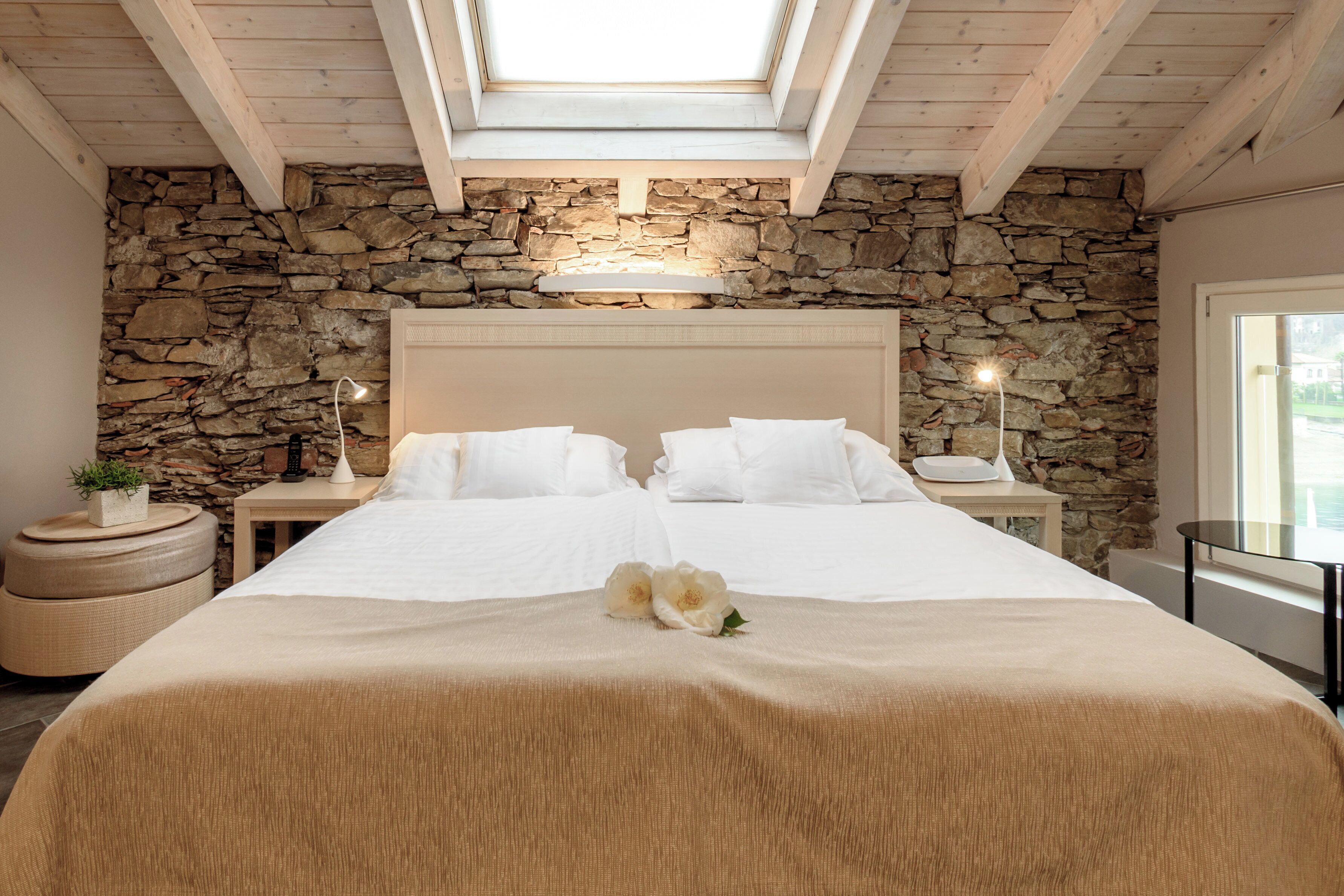 Ein Schlafzimmer mit Steinwand, einem Oberlicht, einem großen Bett, Nachttischen und einem Fenster.
