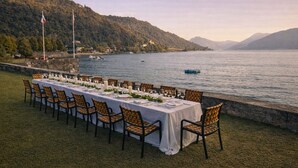 A table set for dining with chairs, overlooking a lake with boats and hills in the background. - Relais Villa Porta (Luino)