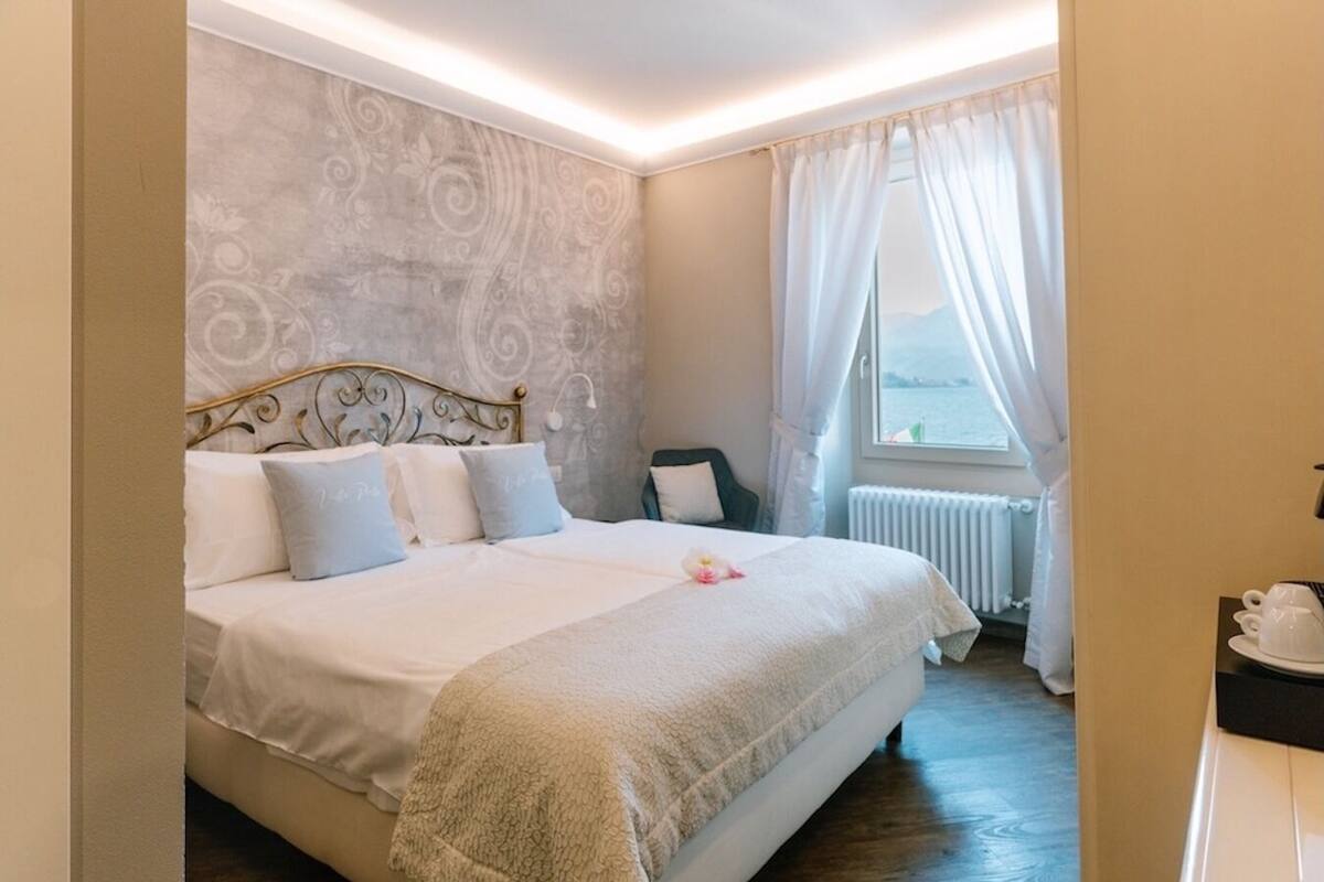 Ein Schlafzimmer mit Bett, Nachttisch, einem Fenster mit Vorhängen und Blick aufs Meer.