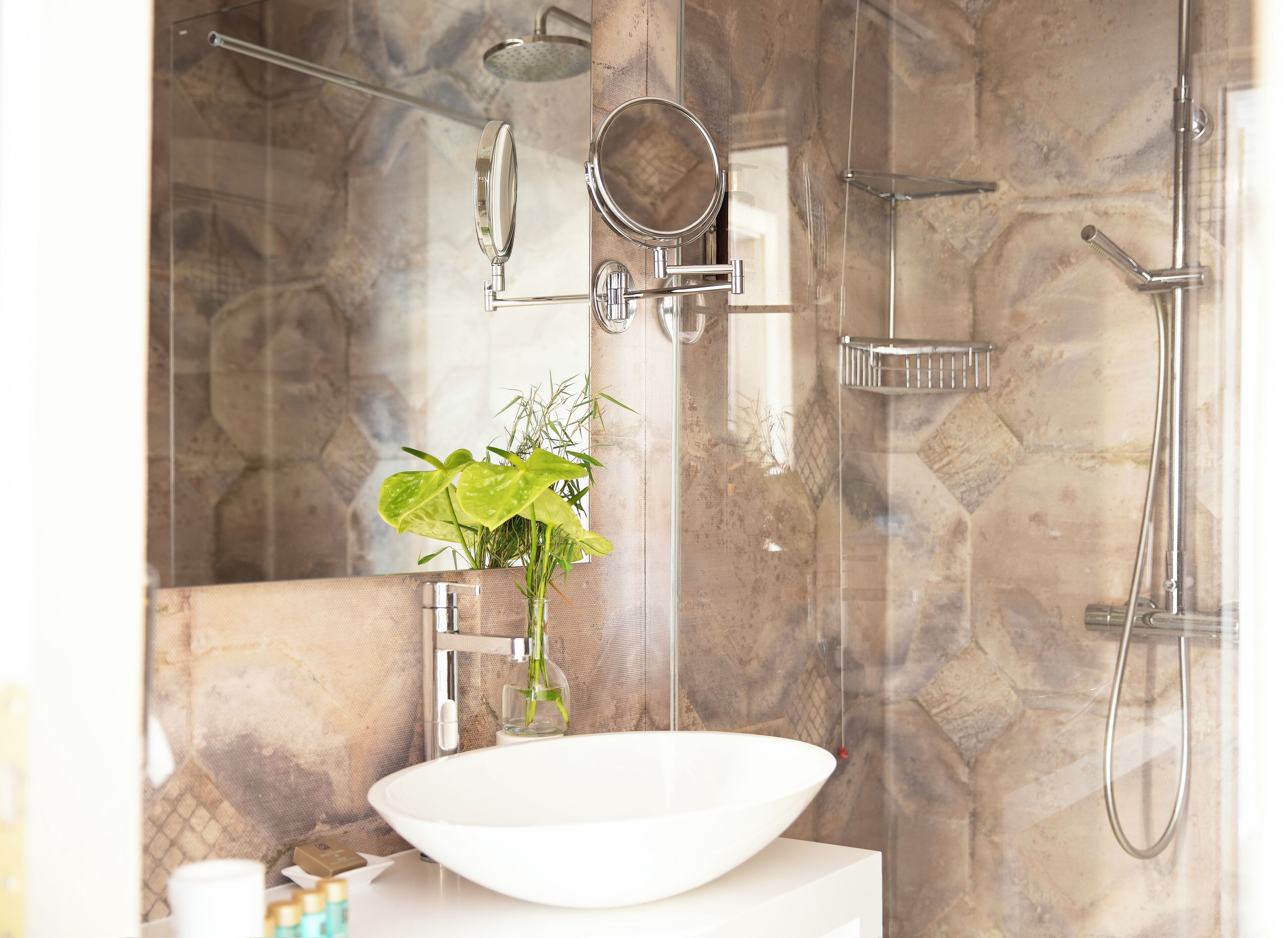A bathroom with a white sink, a mirror, a handheld showerhead, and a glass-enclosed shower.