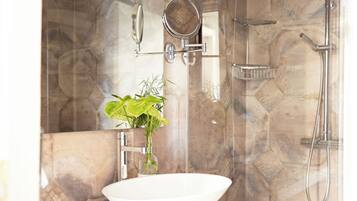 A bathroom with a white sink, a mirror, a handheld showerhead, and a glass-enclosed shower.