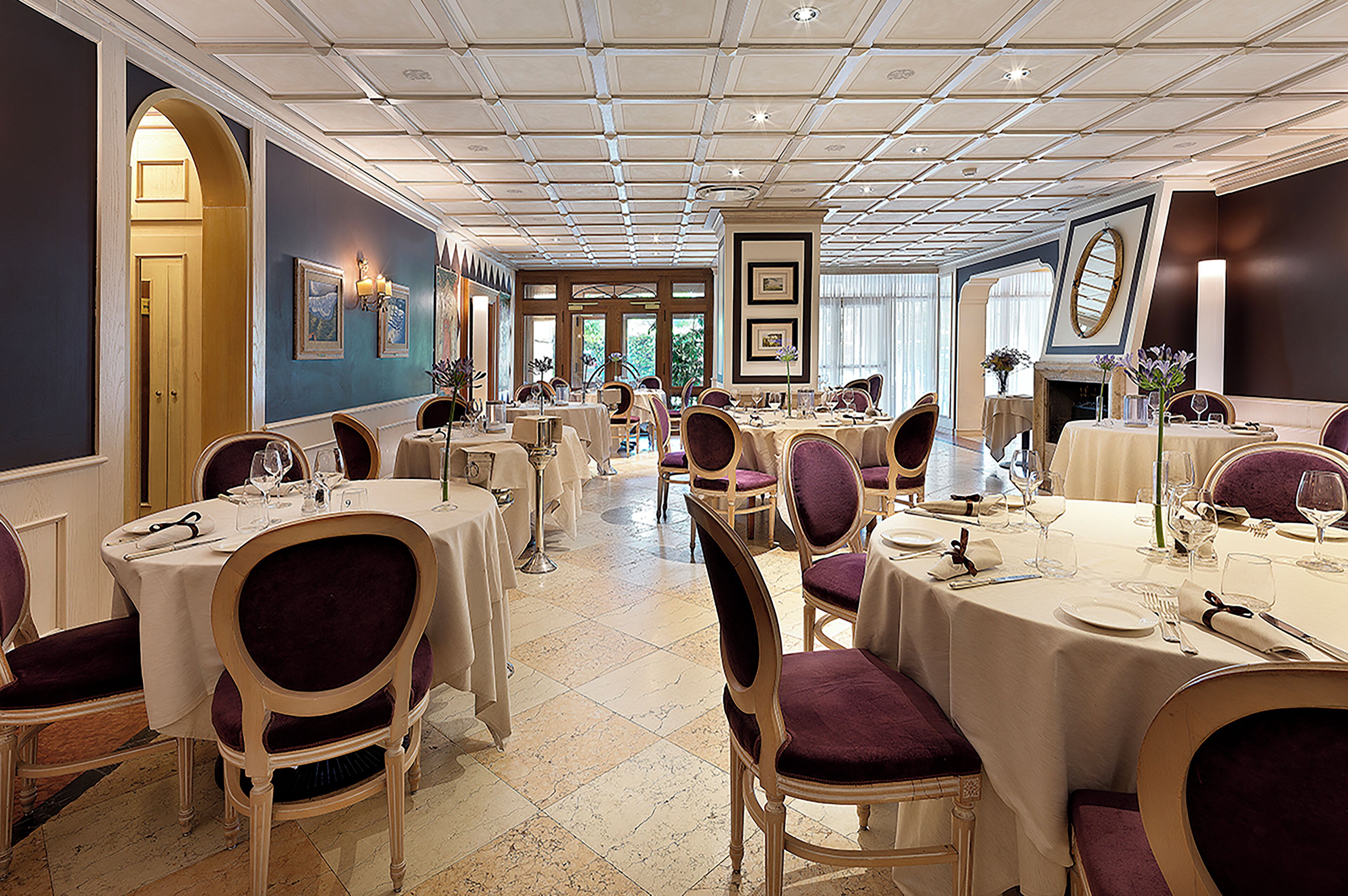 A formal dining room with multiple tables and chairs, a chandelier, and framed artwork on the walls.