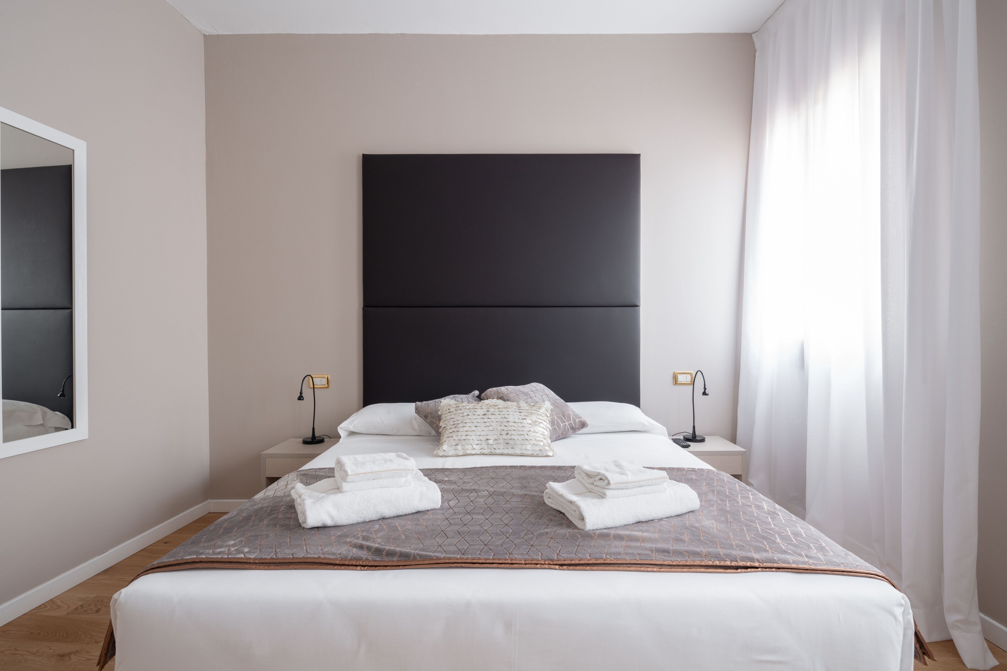 A modern bedroom with a large bed, two bedside tables, a headboard, and a mirror on the wall.