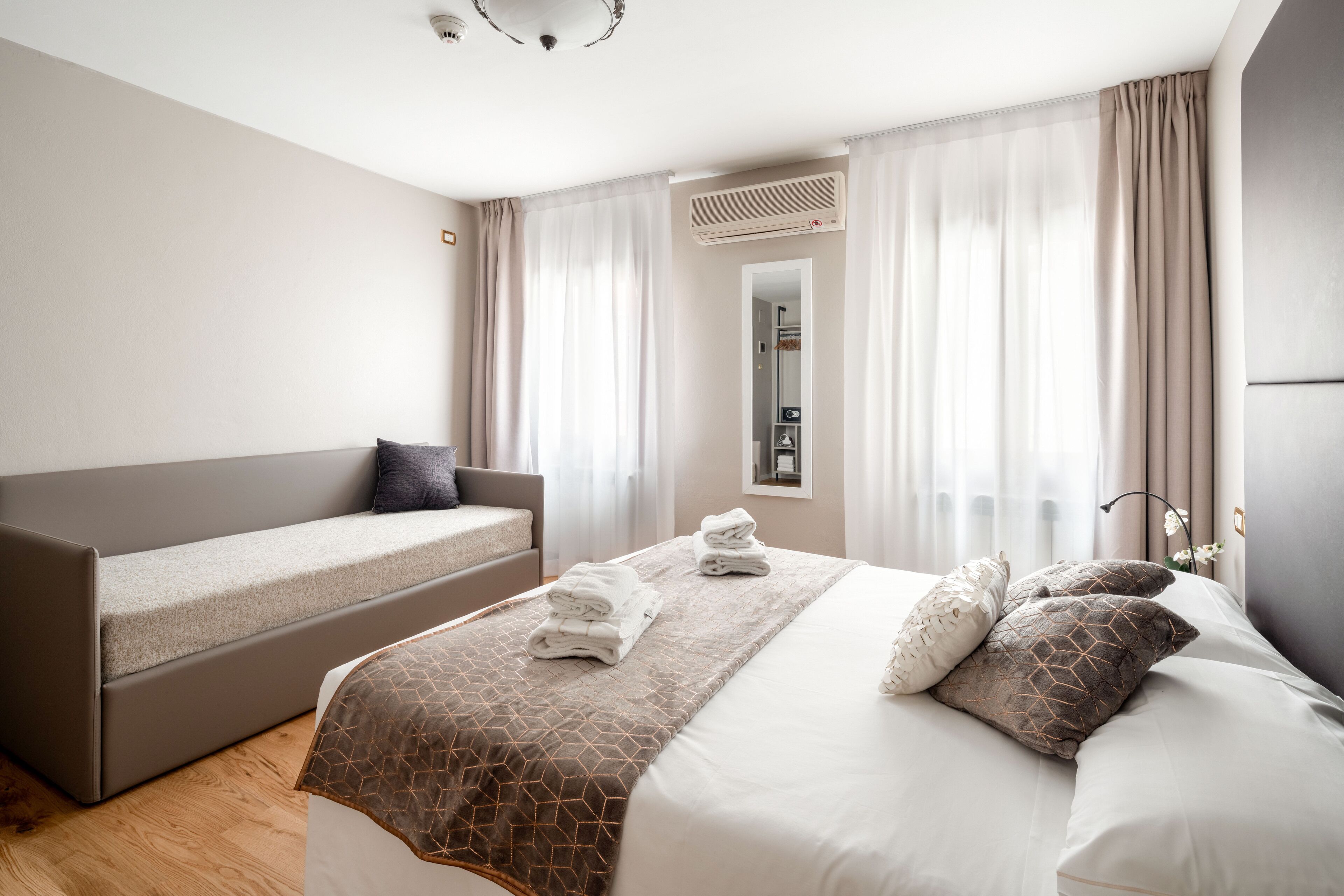 A modern hotel room with a bed, a sofa, and a mirror.
