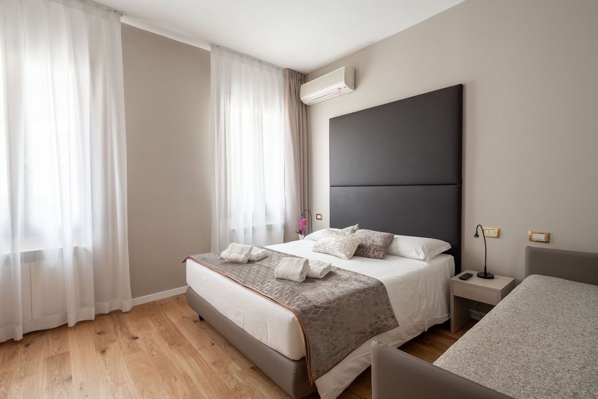 A modern hotel room with a large bed, a bedside table with a lamp, and a small bedside table with a phone.