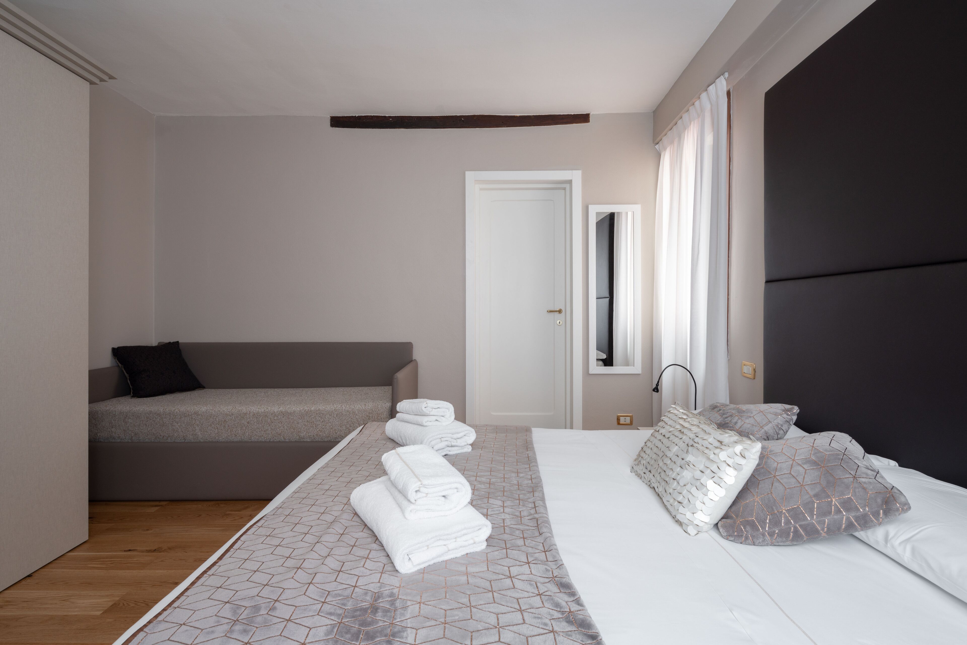 A modern bedroom with a bed, a sofa, and a neatly made bed with towels.