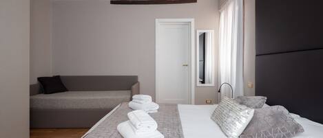 A modern bedroom with a bed, a sofa, and a neatly made bed with towels.