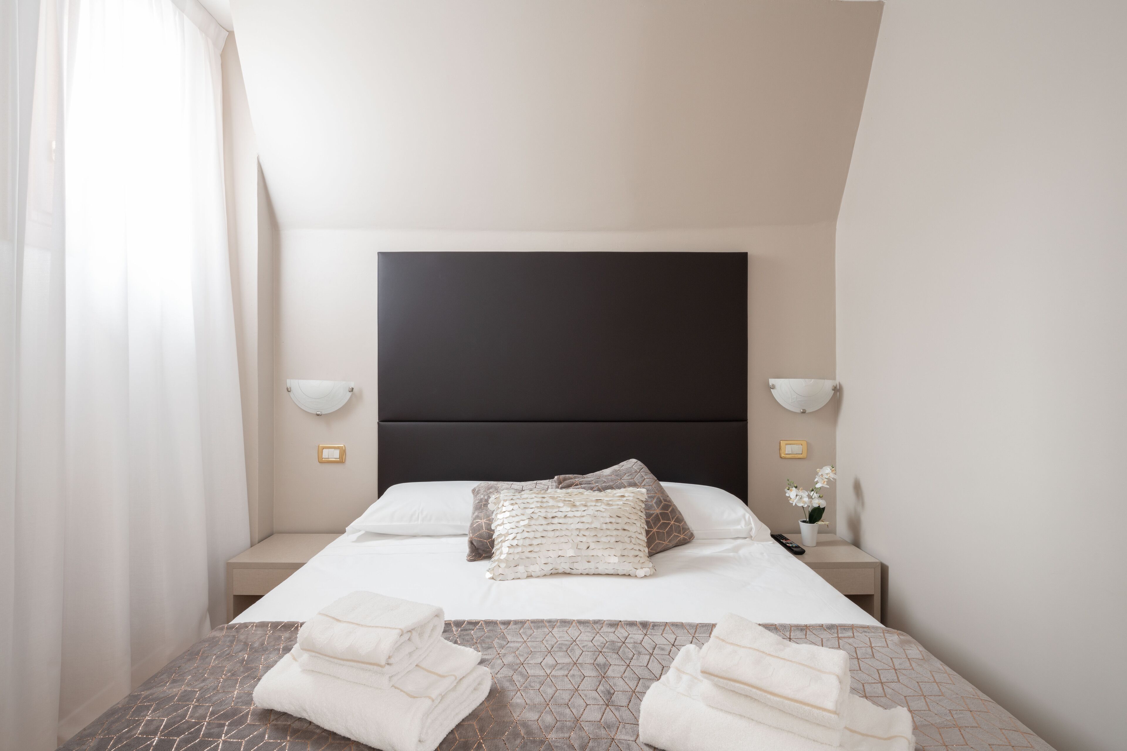 Ein Hotelzimmer mit einem großen Bett, zwei Nachttischen, einem Kopfteil und einem Fenster mit Vorhängen.