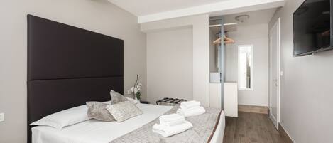 Una habitación de hotel moderna con una cama grande, un televisor de pantalla plana, un vestidor y un baño con espejo y perchero.
