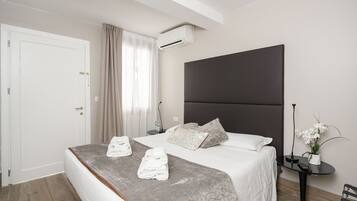 Habitación de hotel moderna con una cama grande, una mesita de noche, un equipo de aire acondicionado, una pequeña mesa con un florero y una silla.