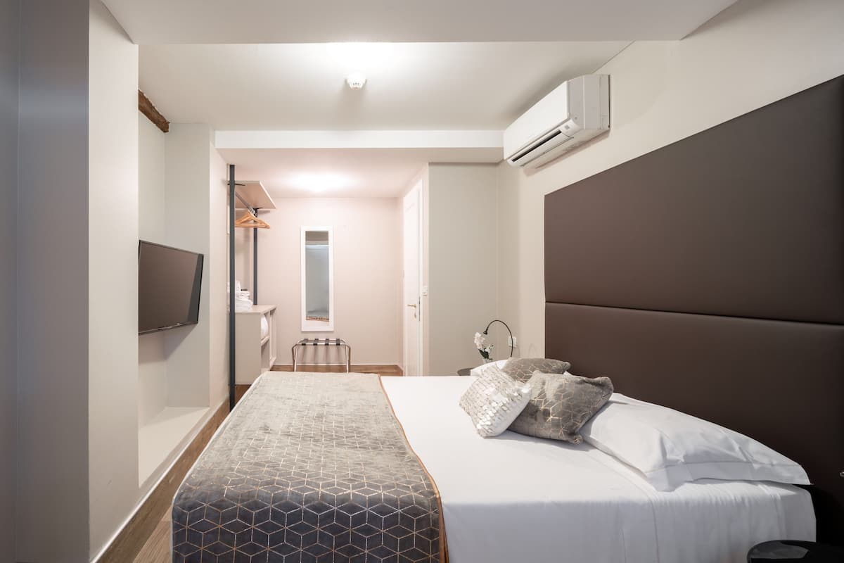 A modern hotel room with a large bed, a flat-screen TV, and an air conditioning unit on the wall.