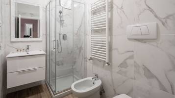 Un baño moderno con ducha de vidrio, un bidé, un inodoro y un lavamanos con espejo.