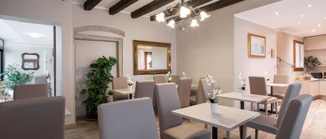 Un restaurant amb sostres alts, bigues descobertes i un lampadari. Taules i cadires disposades per dinar.