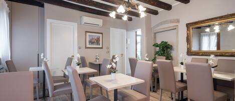 A dining area with wooden beams, white tables, and beige chairs.