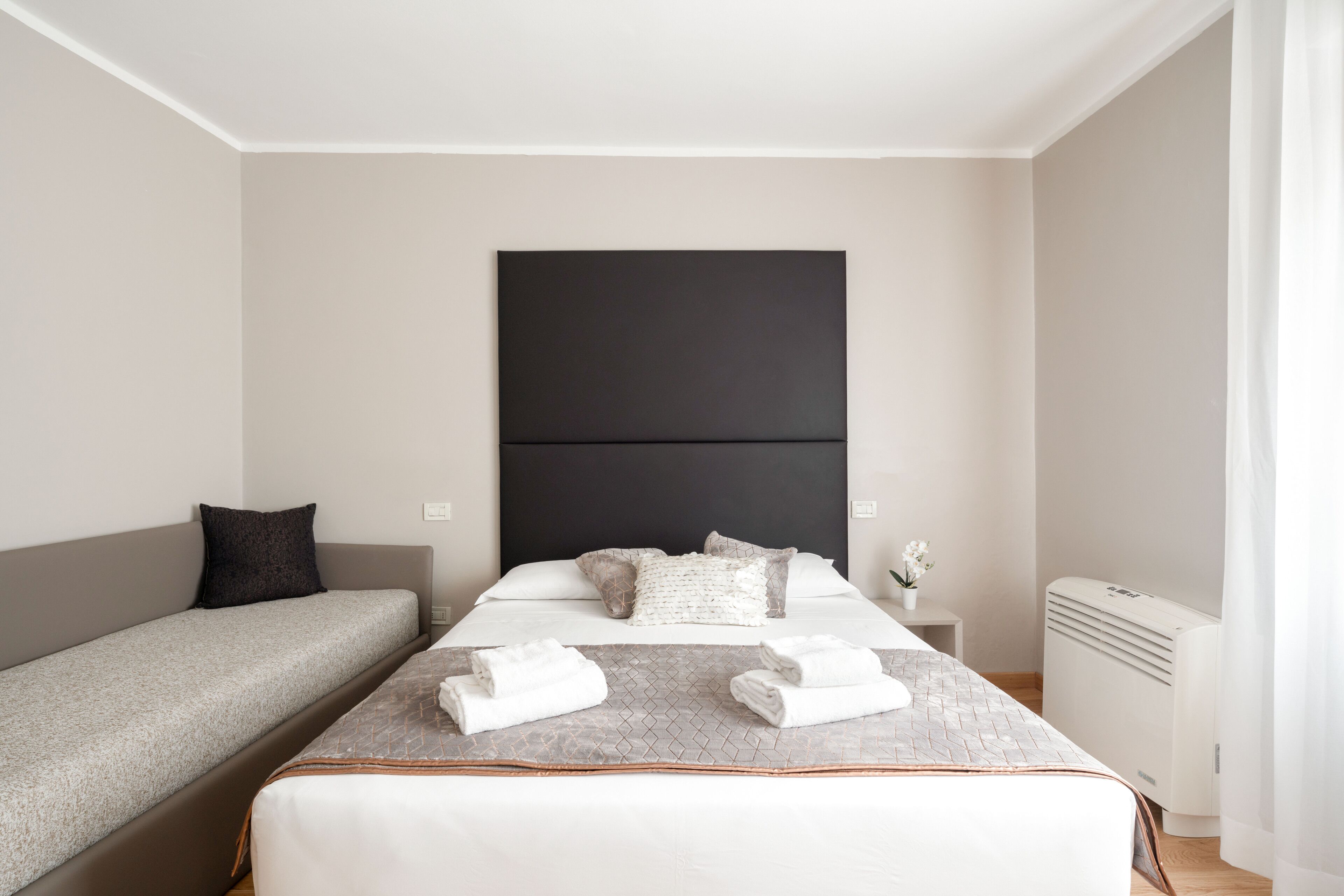 Ein modernes Hotelzimmer mit einem großen Bett, einer kleineren Couch und einem Nachttisch mit Lampe.