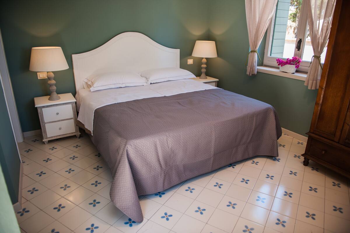 A bedroom with a bed, nightstands, a window with curtains, and a wooden dresser.