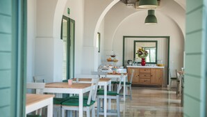 Un comedor con mesas y sillas blancas, un armario de madera y un espejo sobre el mostrador.