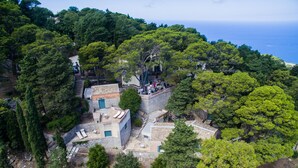 Vista aérea de una propiedad costera con un edificio de piedra, asientos exteriores y vistas al mar.