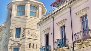 A building with a corner tower featuring a statue, multiple windows, and balconies with metal railings. - Hotel Posta (Syracuse)