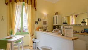 A bright kitchen with a dining area, featuring a table, chairs, a counter, and a window with curtains. - Hotel Posta (Syracuse)