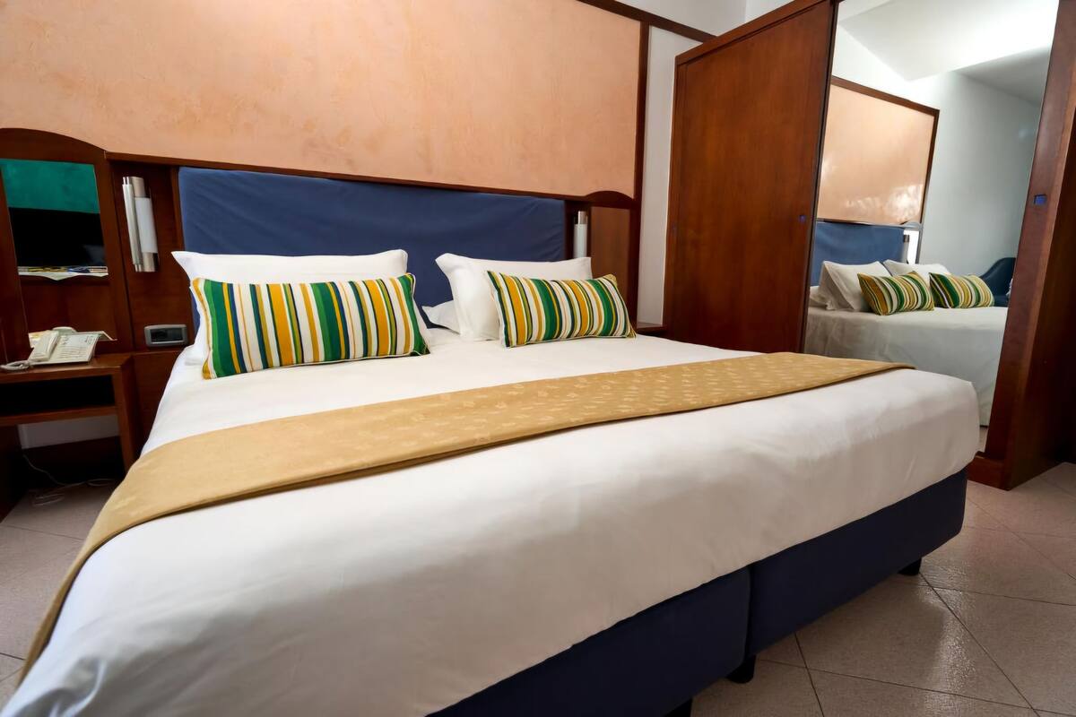 A hotel room with a large bed, a wooden headboard, a bedside table with a phone, and a mirror.