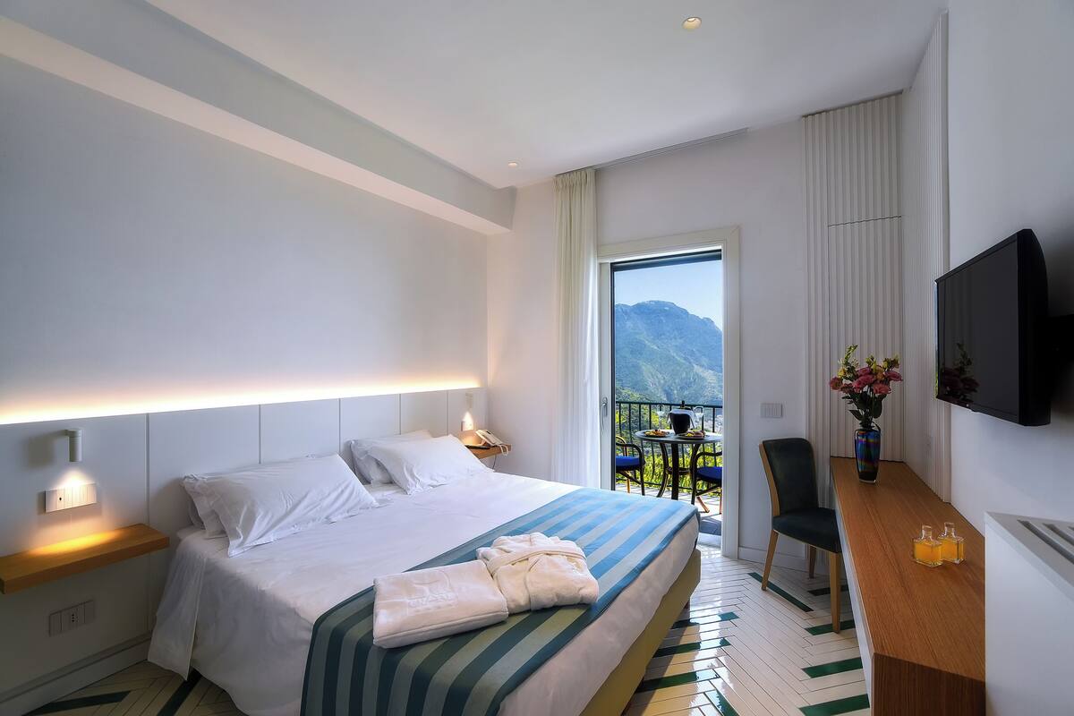 A modern hotel room with a large bed, bedside table, and a TV.