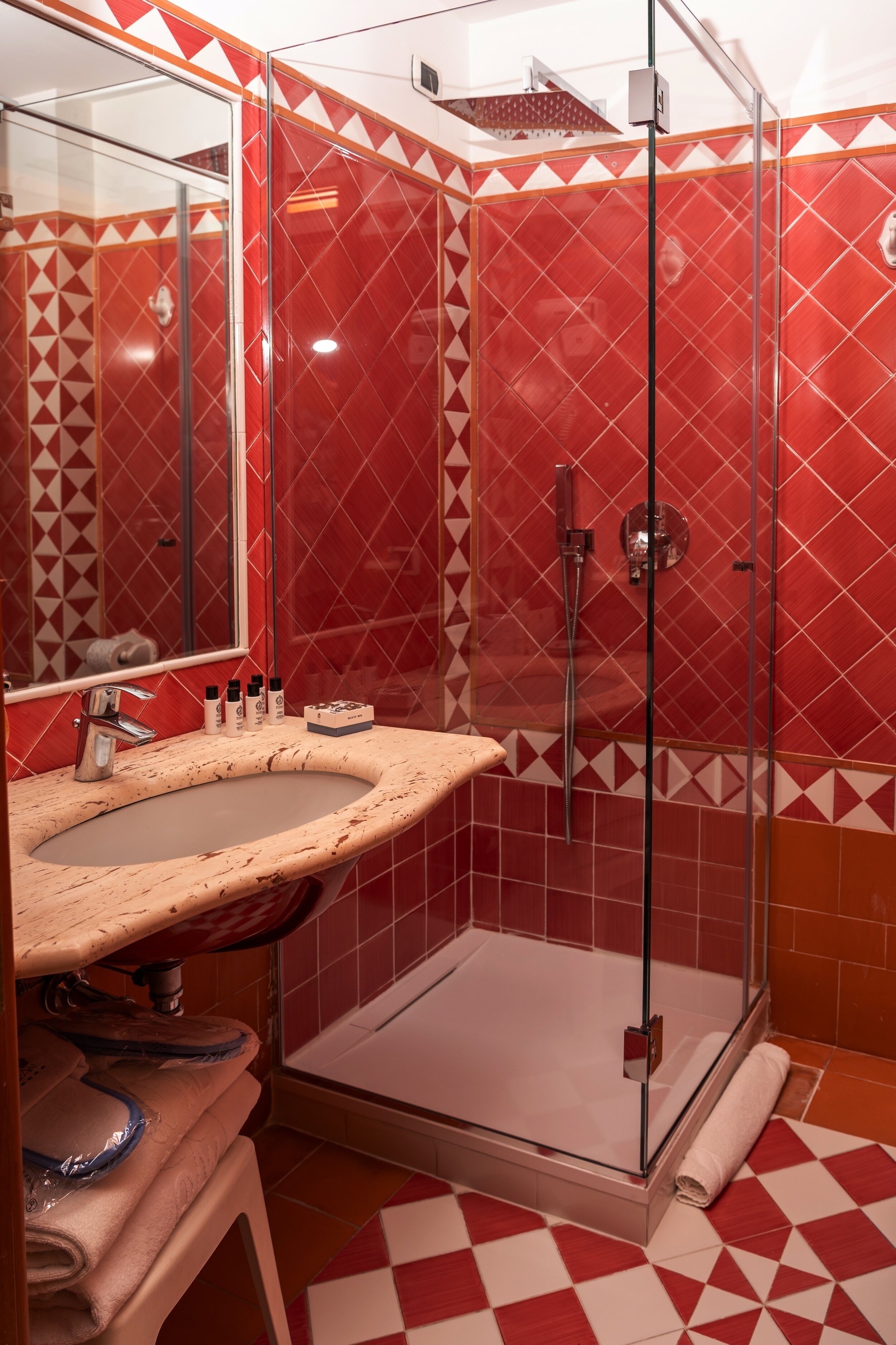 Un bagno con doccia vetro e piastrelle rosse decorate.