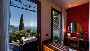 A balcony with a table set for two, a wooden dresser, and a view of the sea and mountains. - Hotel Graal (Ravello)