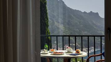 A balcony with a table set for a meal, overlooking a mountainous landscape.