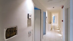 A hotel hallway with a white floor, doors numbered 147 and 152, and a blue door at the end. - Hotel Graal (Ravello)