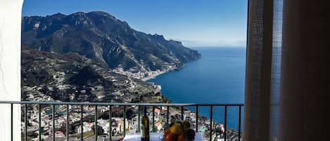 A balcony with a table, chairs, and a view of a coastal landscape with mountains and the sea.
