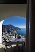 A balcony with a table, chairs, and a view of a coastal landscape with mountains and the sea.