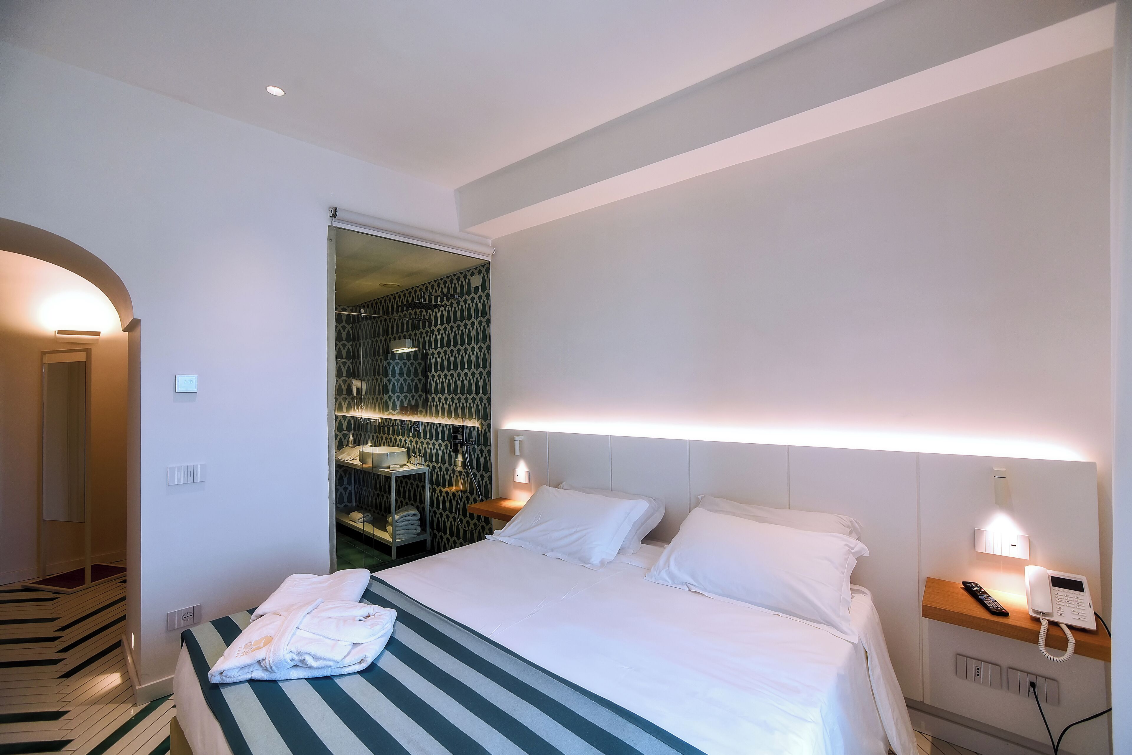 Ein Hotelzimmer mit Bett, Nachttisch mit Telefon und begehbarem Kleiderschrank mit gemustertem Wandpapier.