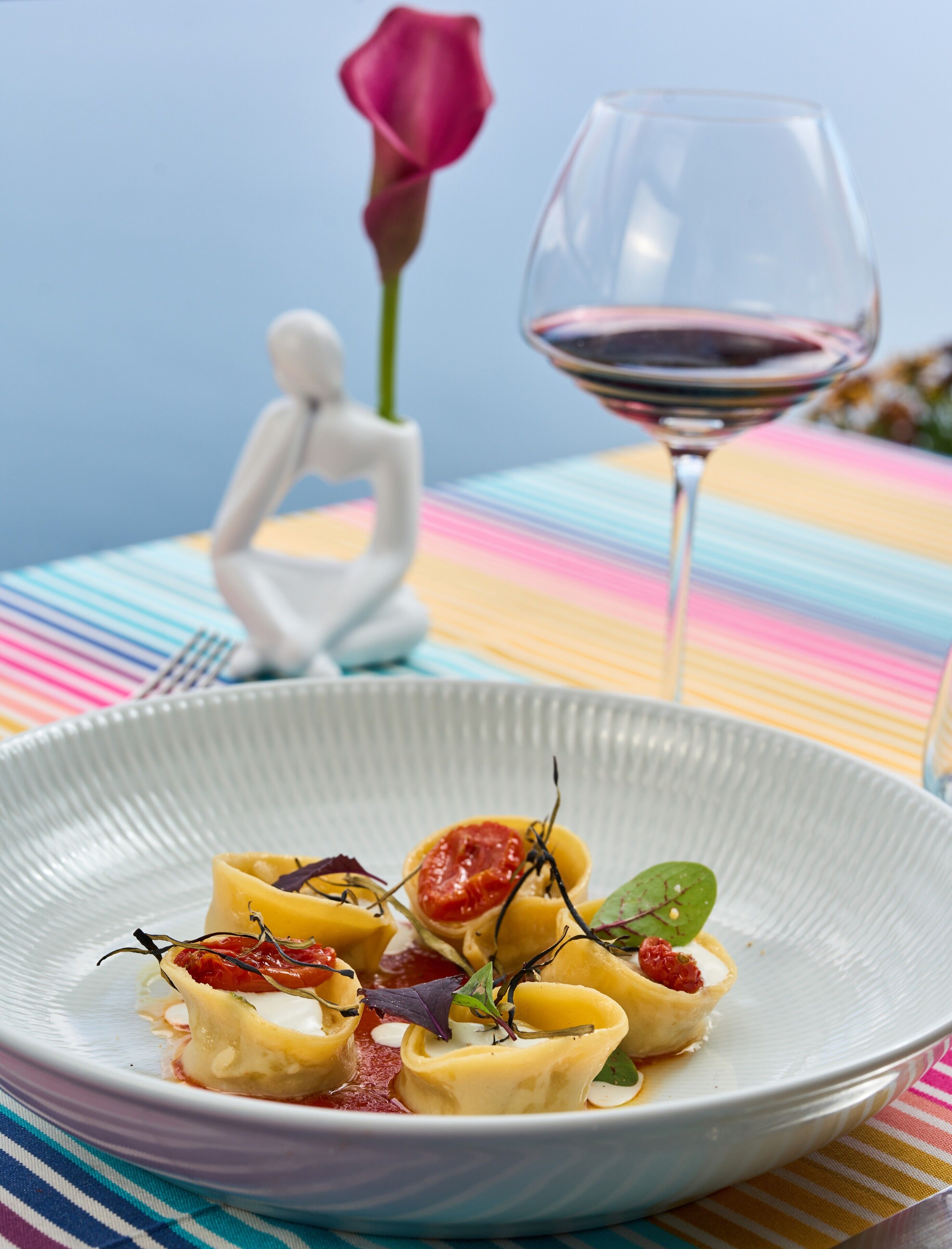 Une assiette de pâtes aux tomates cerises et aux légumes verts, un verre de vin rouge et une rose rose en arrière-plan.