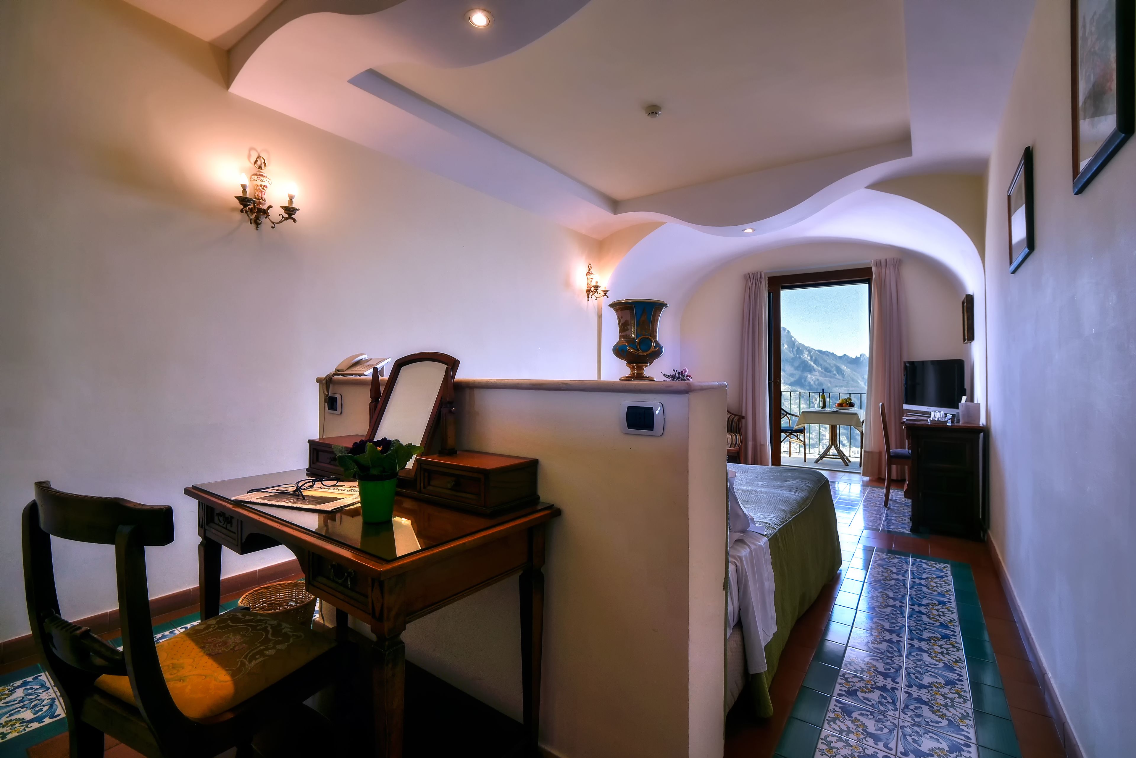 Une chambre d’hôtel équipée d’un bureau, d’une chaise, d’un lit et offrant une vue sur les montagnes par la fenêtre.